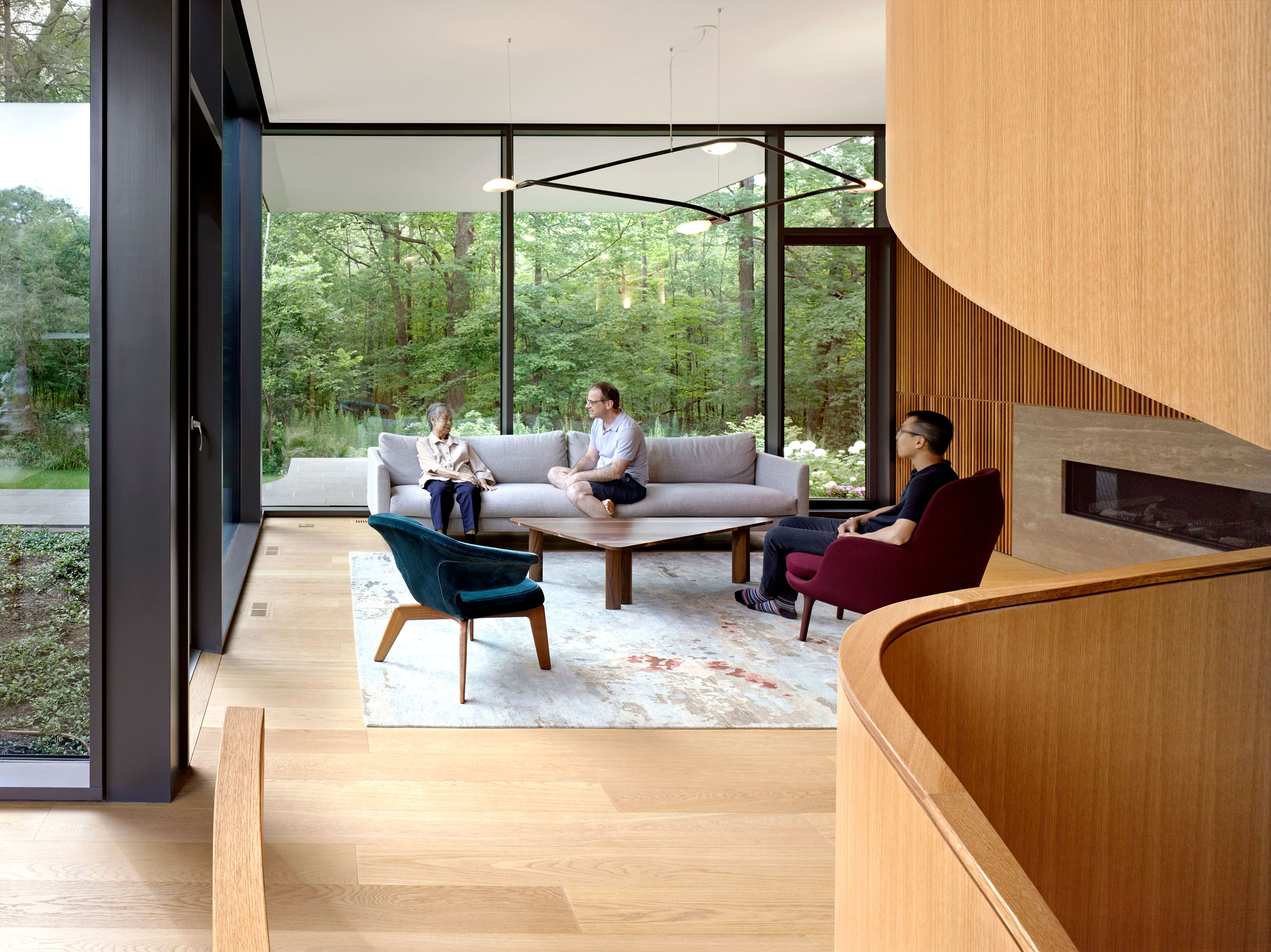 Wohnzimmer mit Naturbezug Alt-Text: Familie im Wohnzimmer mit großer Glasfront und Blick in die Natur im Mehrgenerationenhaus